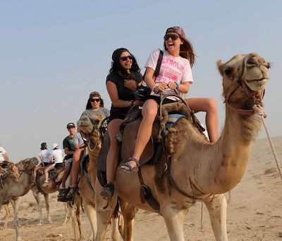 tourist riding camel in ras al khaimah desert for 1 hour with sand surfing, and refreshments on camel ride tour in ras al khaimah