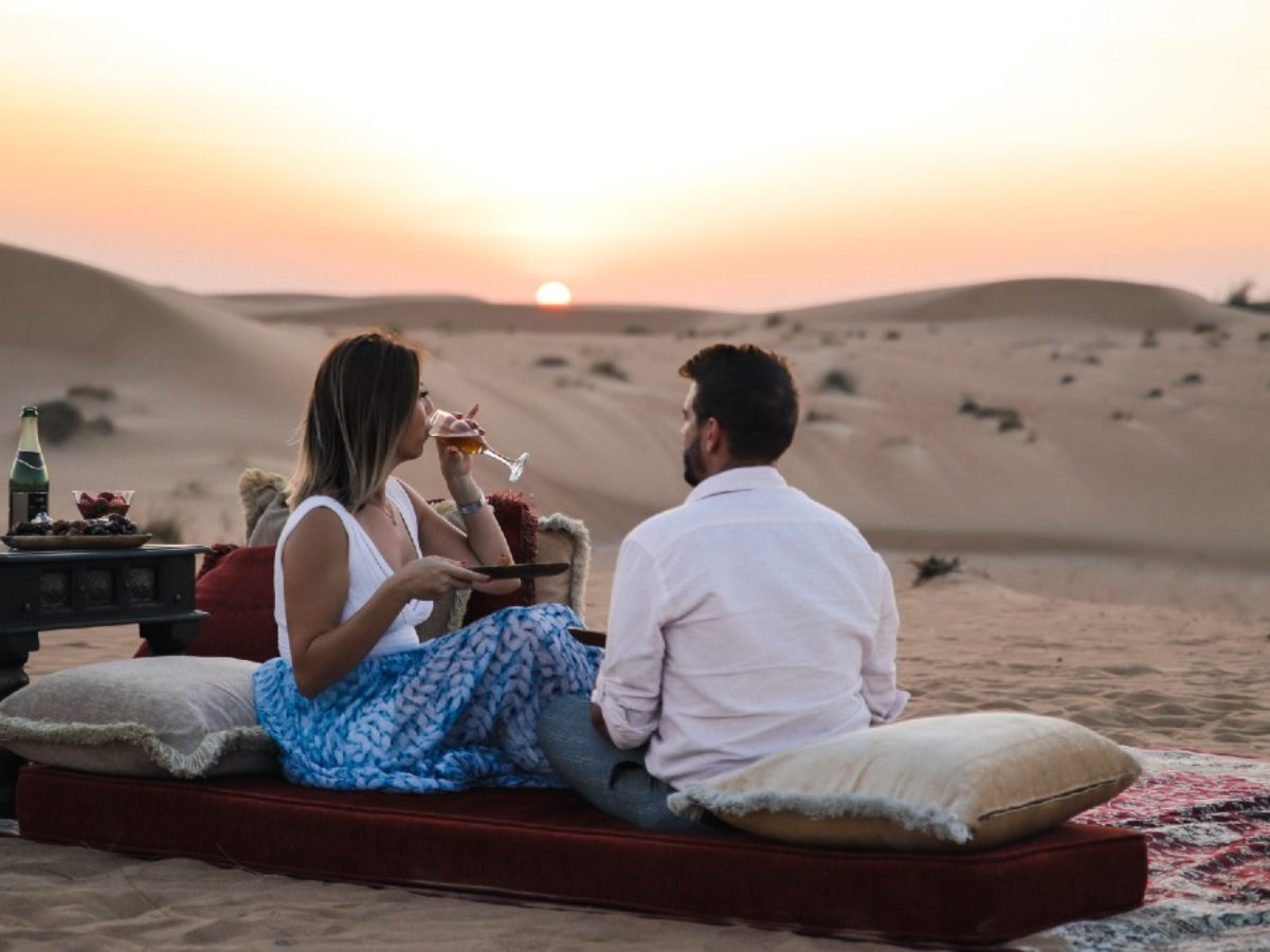 couple tourist enjoying wine, bbq on a private dune with belly dance, tanoura fire spinners and camels rides from Desert safari from Ras Al Khaimah